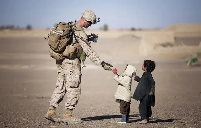 A soldier giving a gift to two kids.