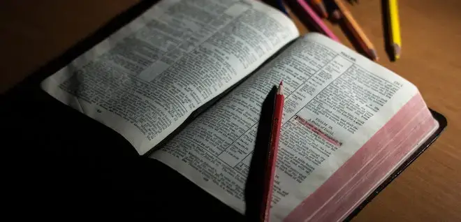 An open bible with marker pencils surrounding it.