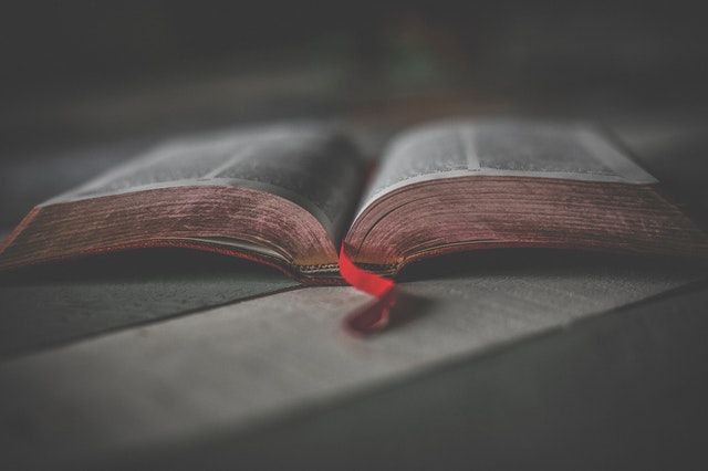 Open Bible on a table with a red ribbon separating the pages