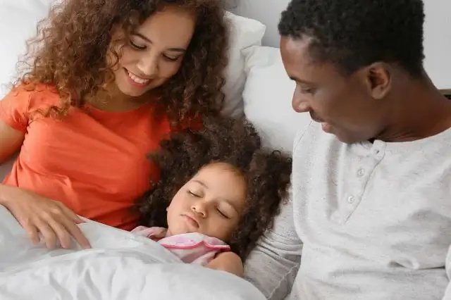 Photo of a couple lying in bed with their sick daughter in the middle