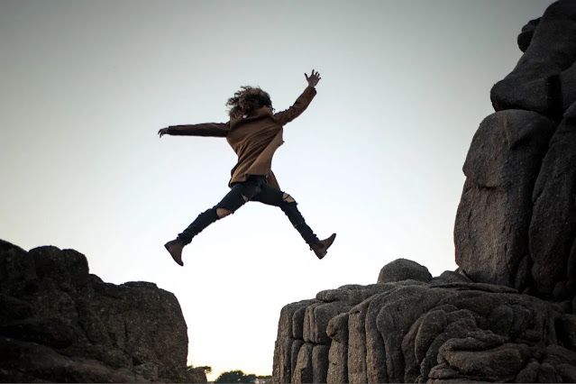 A young lady fearlessly jumping between rock spaces