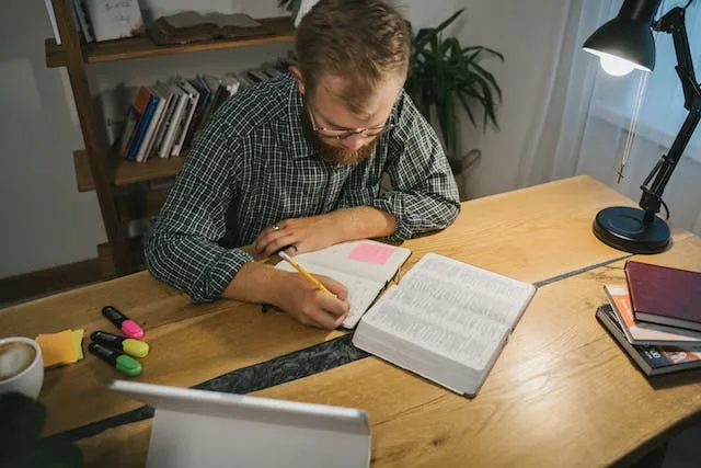 a man engaged in deep bible study in his study desk with a bulb hanging above him
